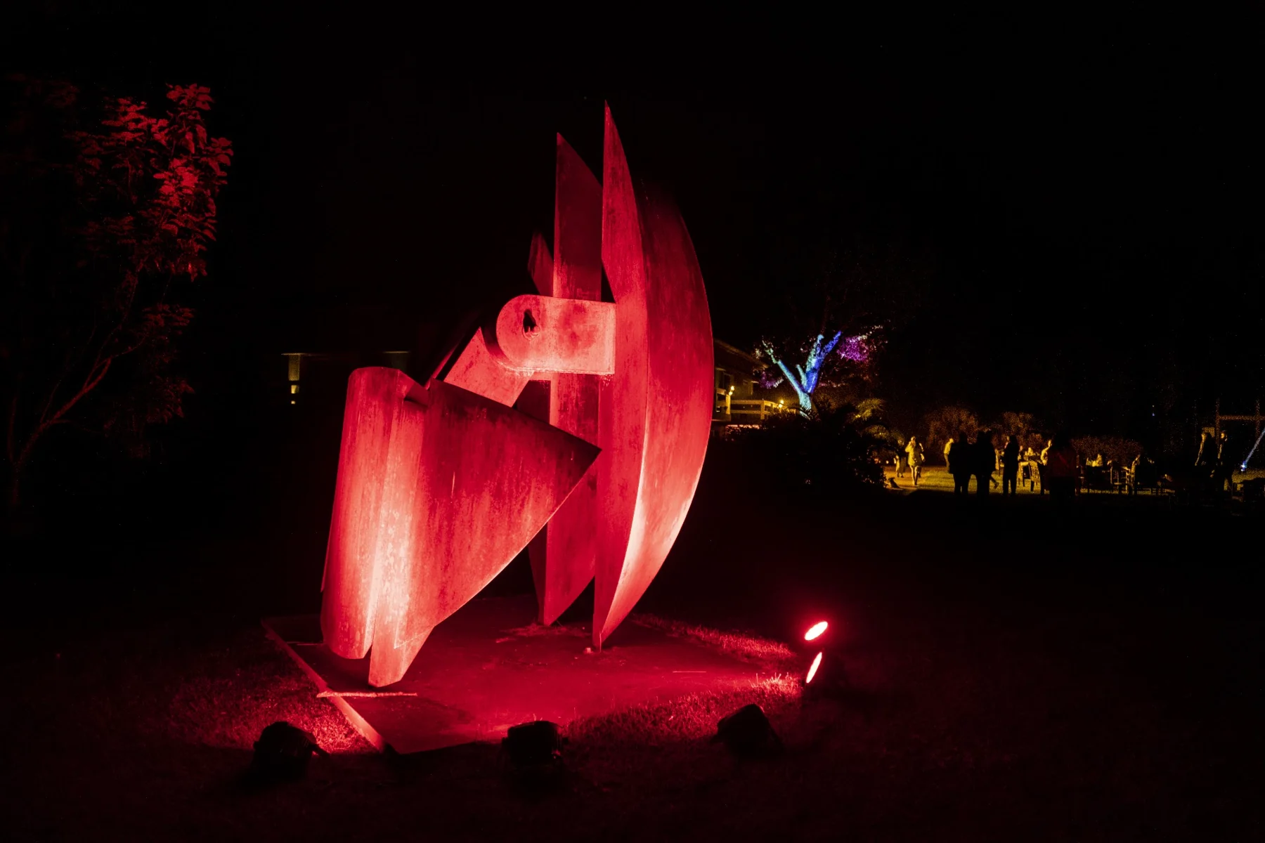 Escultura roja iluminada de noche entre los jardines